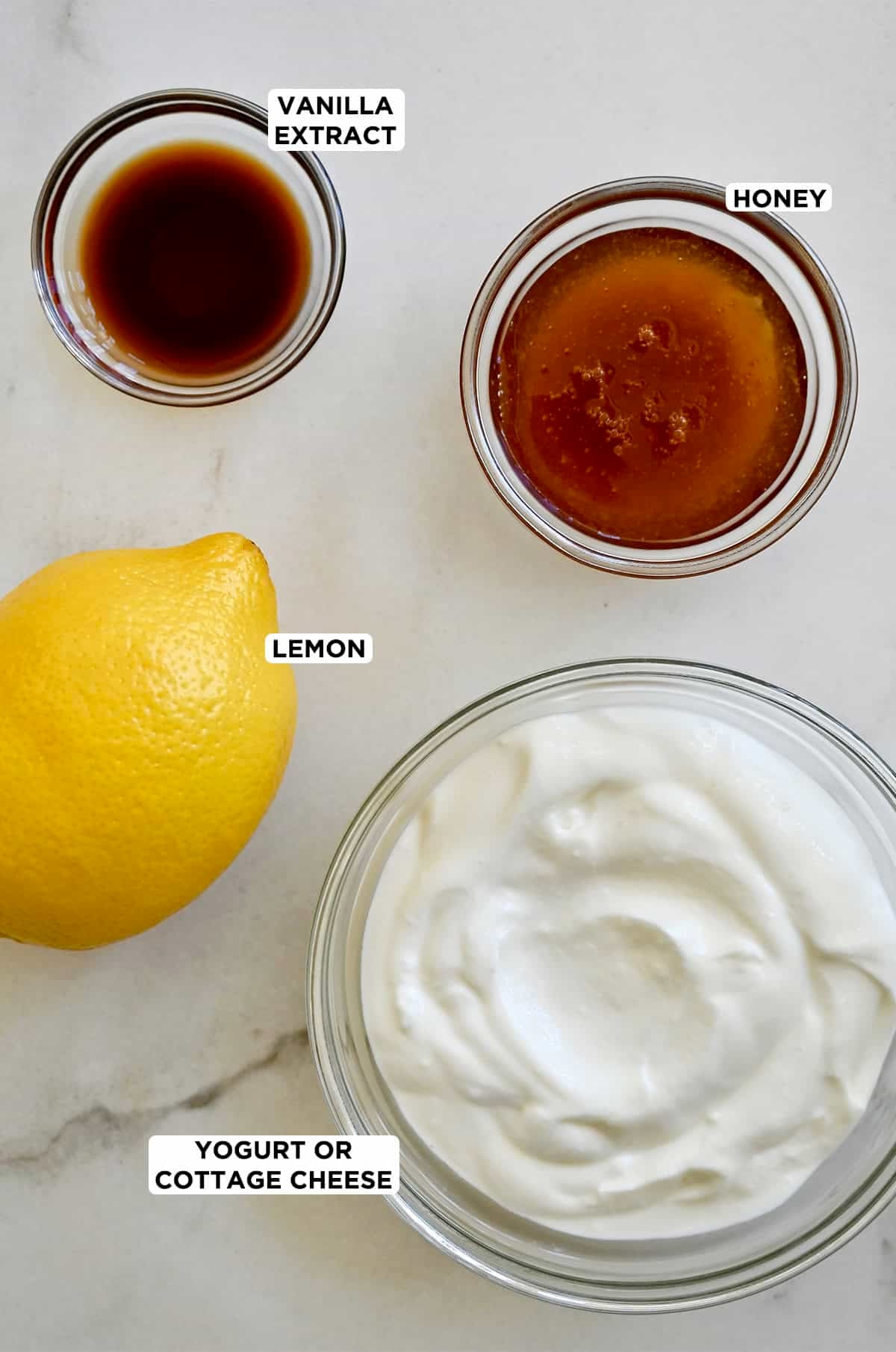 The four ingredients needed to make fruit dip in bowls: vanilla extract, honey, Greek yogurt and a lemon.