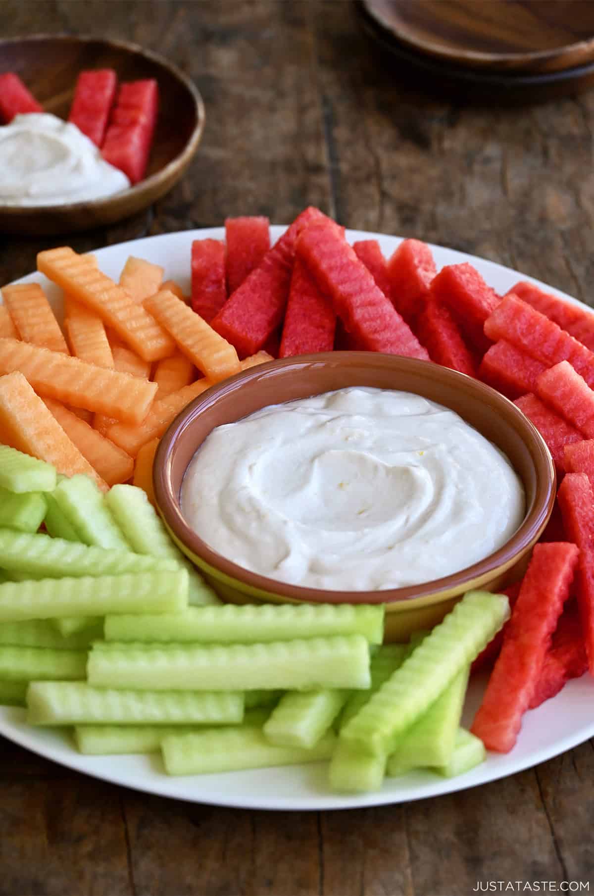 Creamy fruit dip in a small bowl on a plate surrounded by fruit.