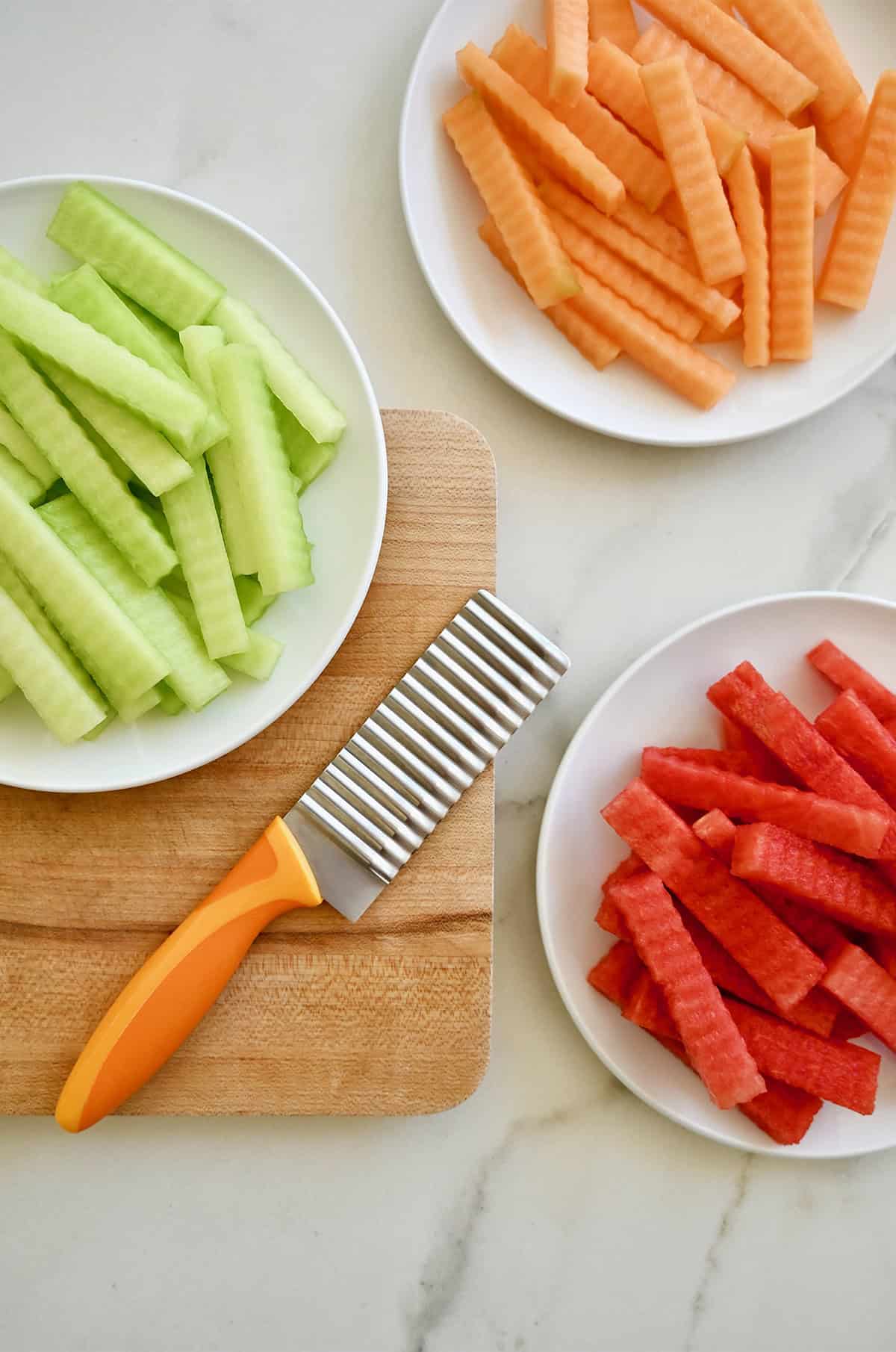 Using a crinkle cut knife to cut strips of watermelon, honeydew and cantaloupe into fruit fries.