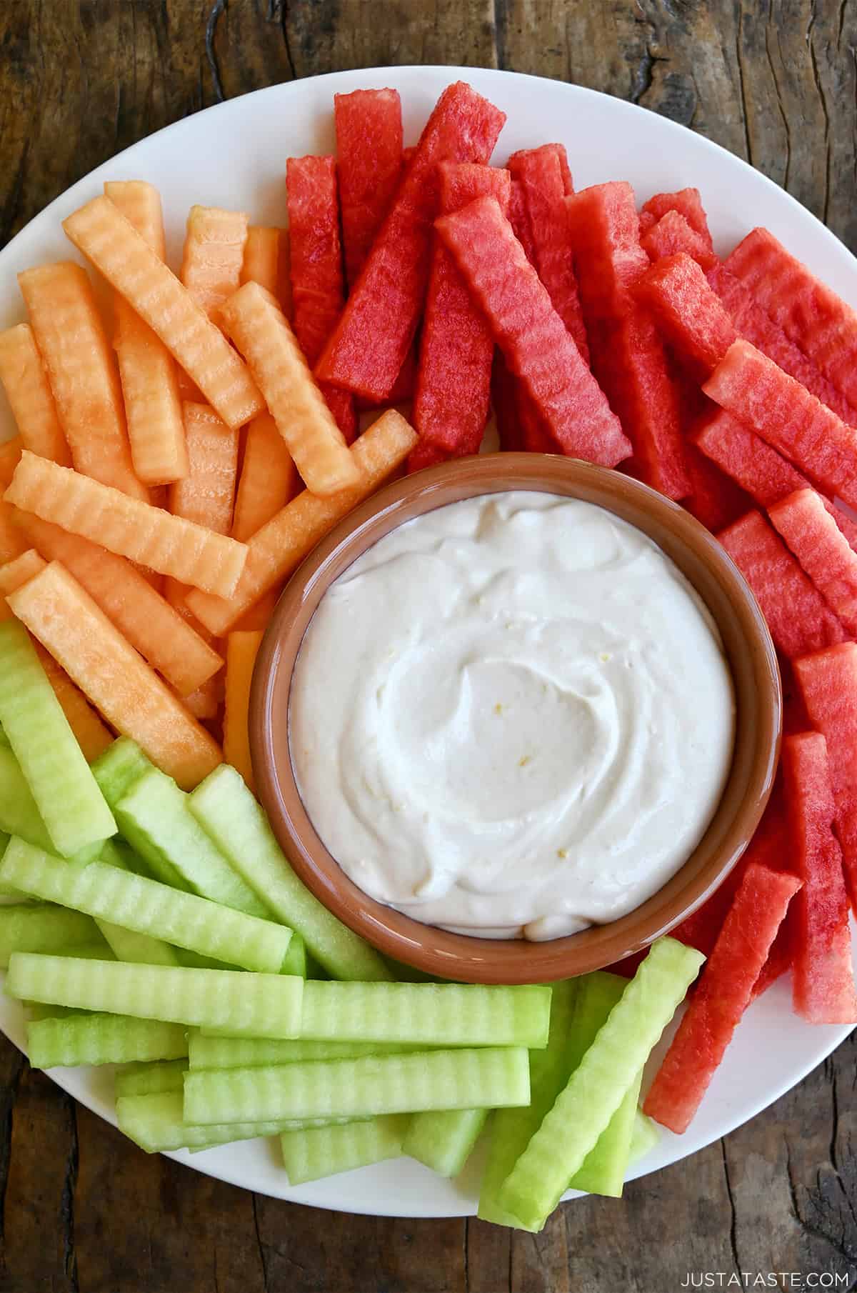 Creamy yogurt fruit dip in a bowl on a plate surrounded by fresh fruit.