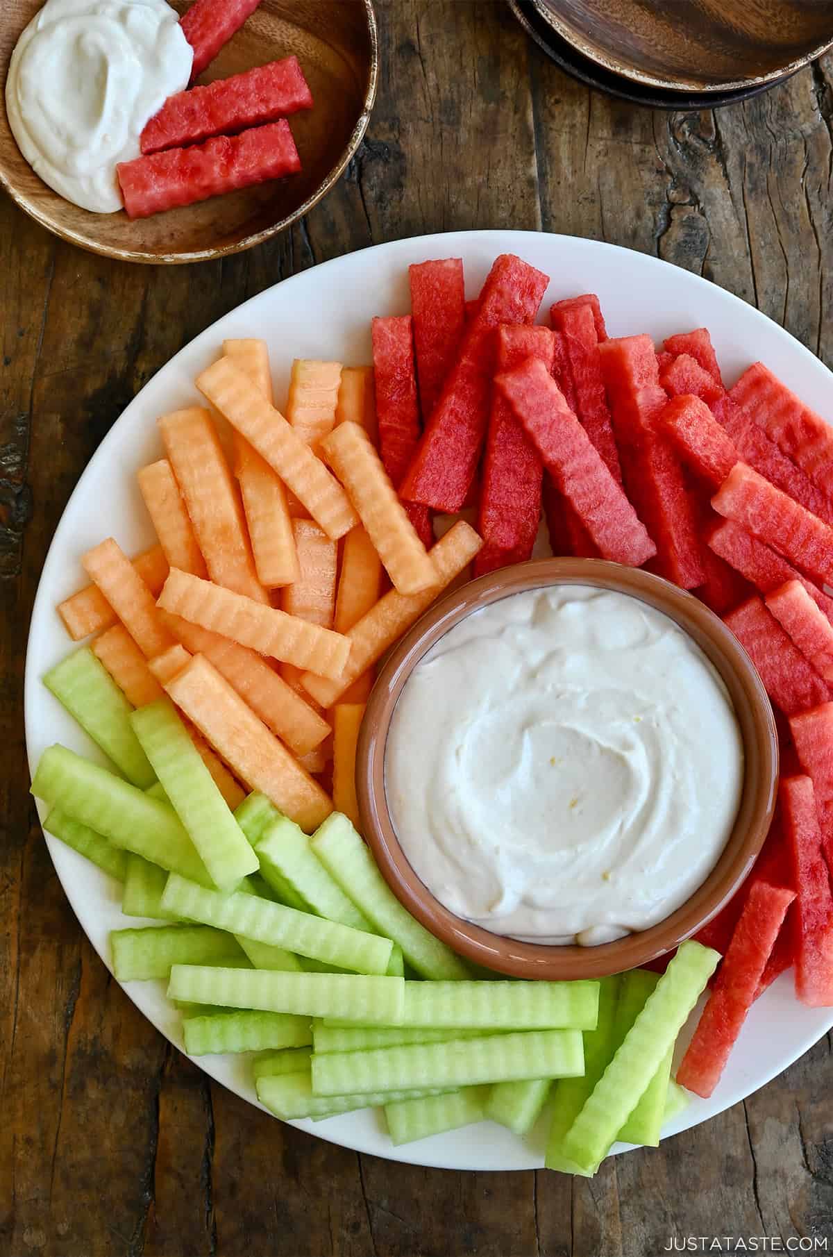 Greek yogurt fruit dip in a small bowl on a plate surrounded by a rainbow of fruit.