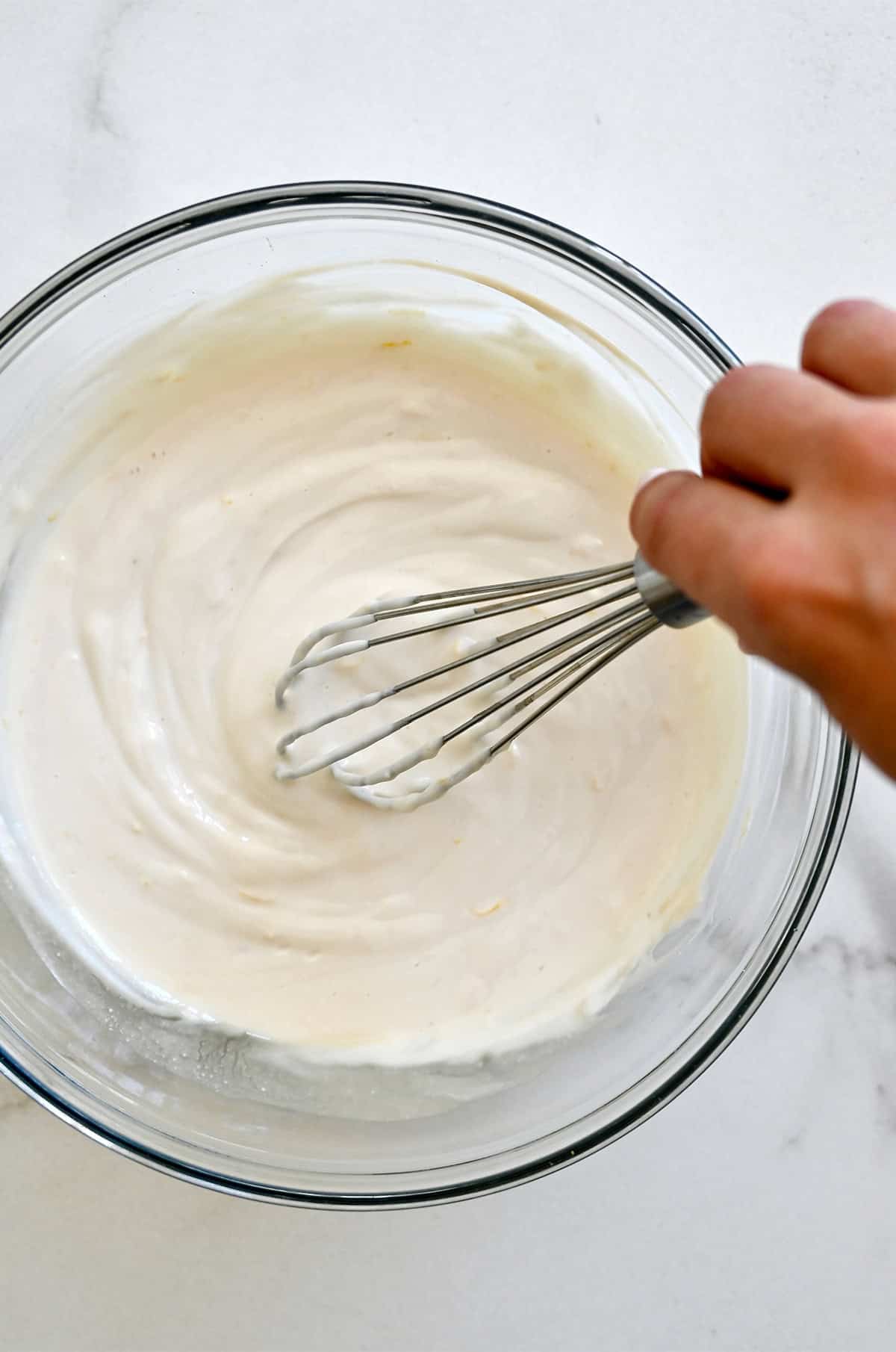 Stirring together a creamy fruit dip with a whisk in a large glass bowl.