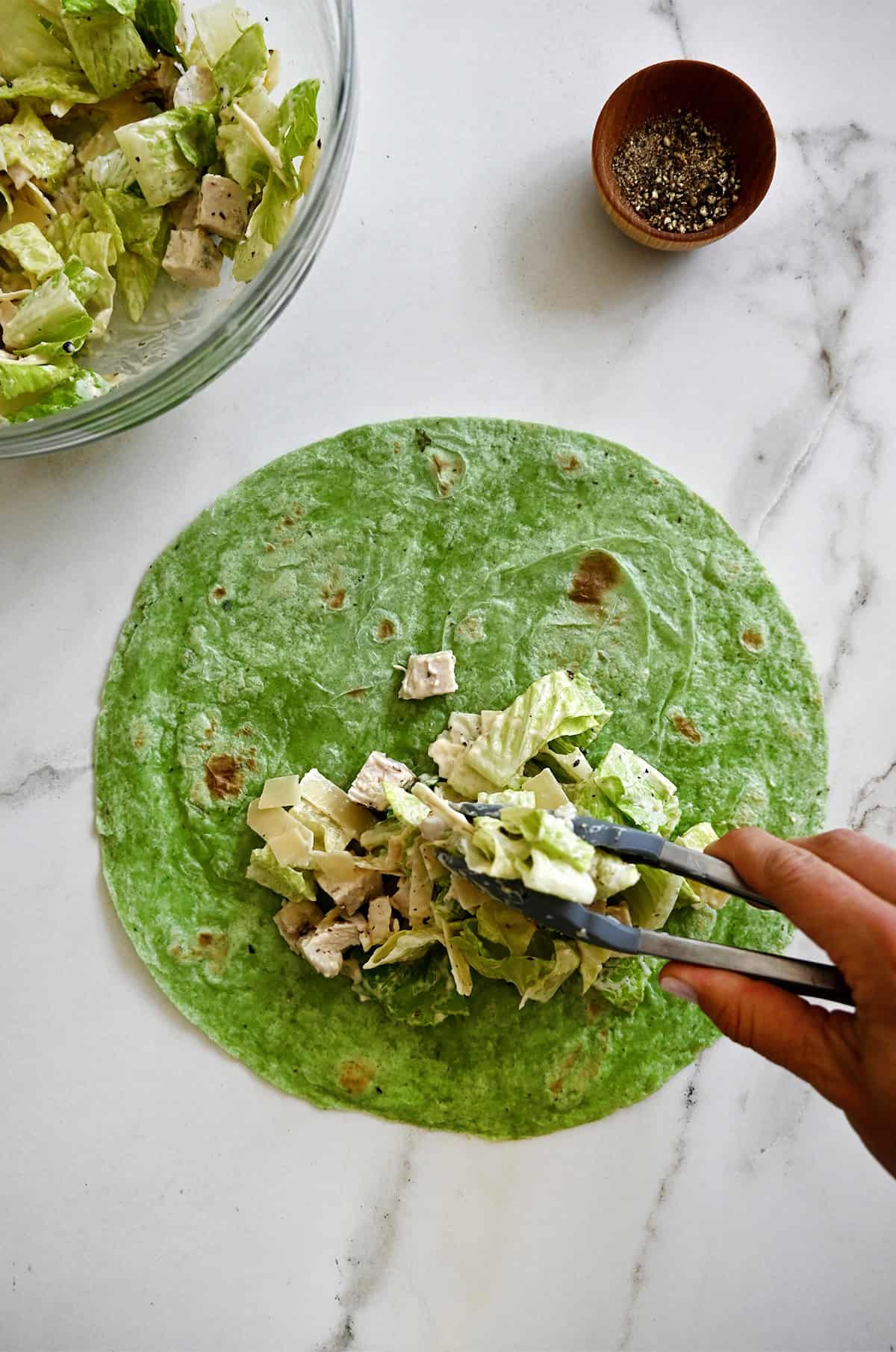 Adding chicken Caesar salad atop a soft spinach wrap.