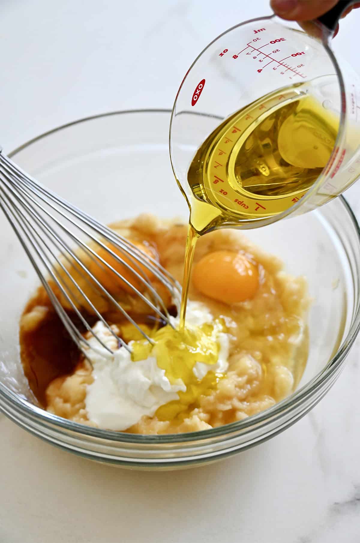 Whisking together the wet ingredients with mashed bananas in a large mixing bowl to make protein banana muffins.