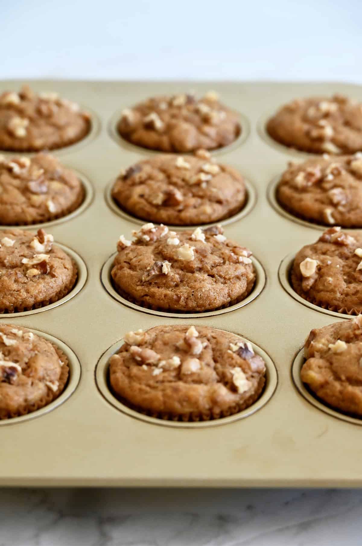 Freshly baked protein banana muffins with chopped walnuts in a muffin tin.