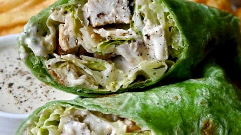 Chicken Caesar salad in a spinach wrap on a plate with French fries and a small bowl containing Caesar dressing.
