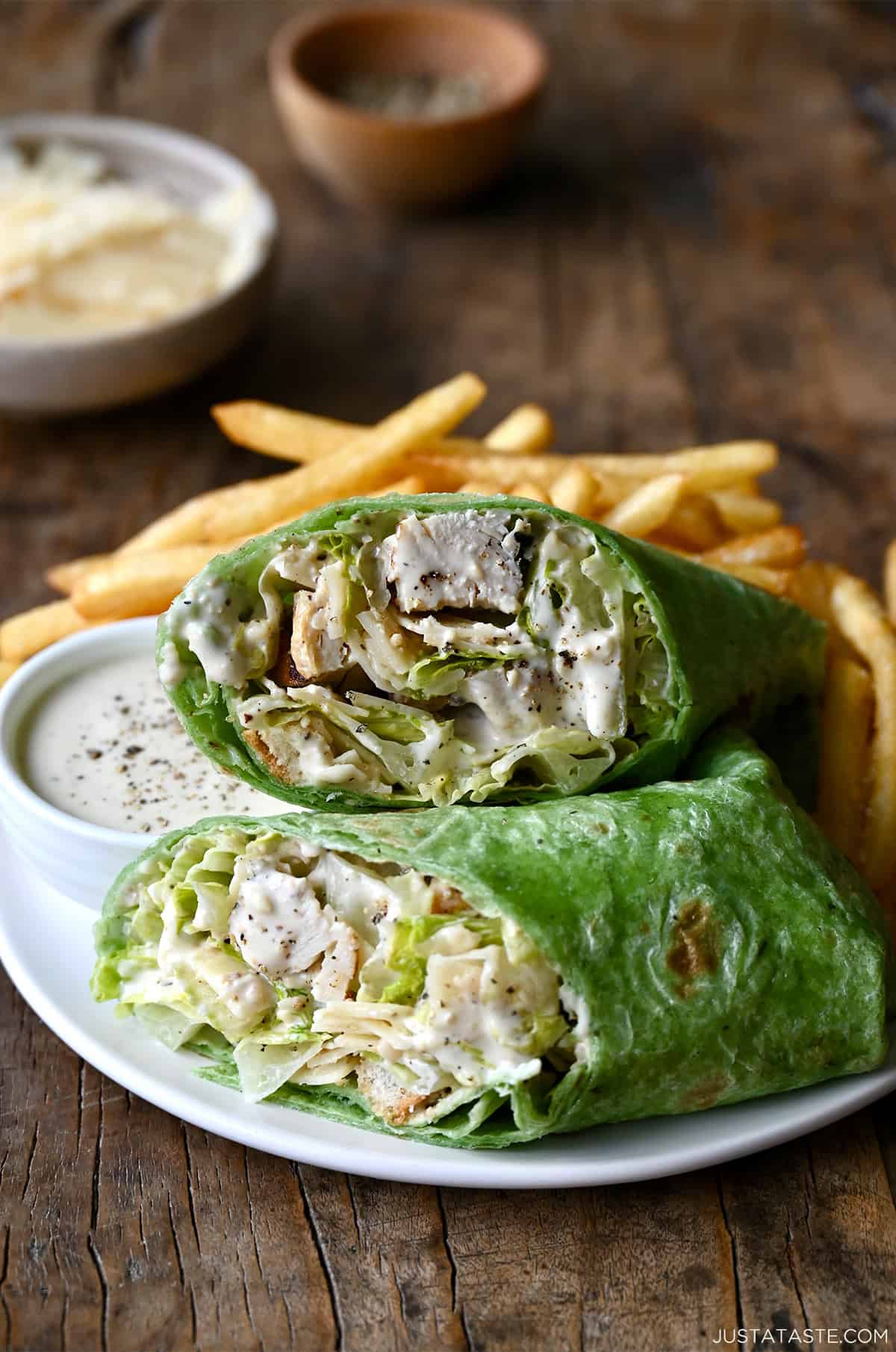 A chicken Caesar wrap cut in half on a plate with French fries.