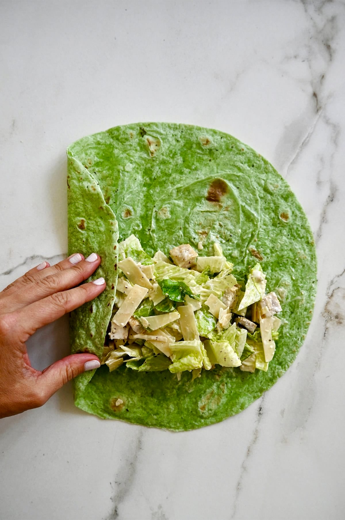 Folding the left side of a large tortilla over Caesar salad.