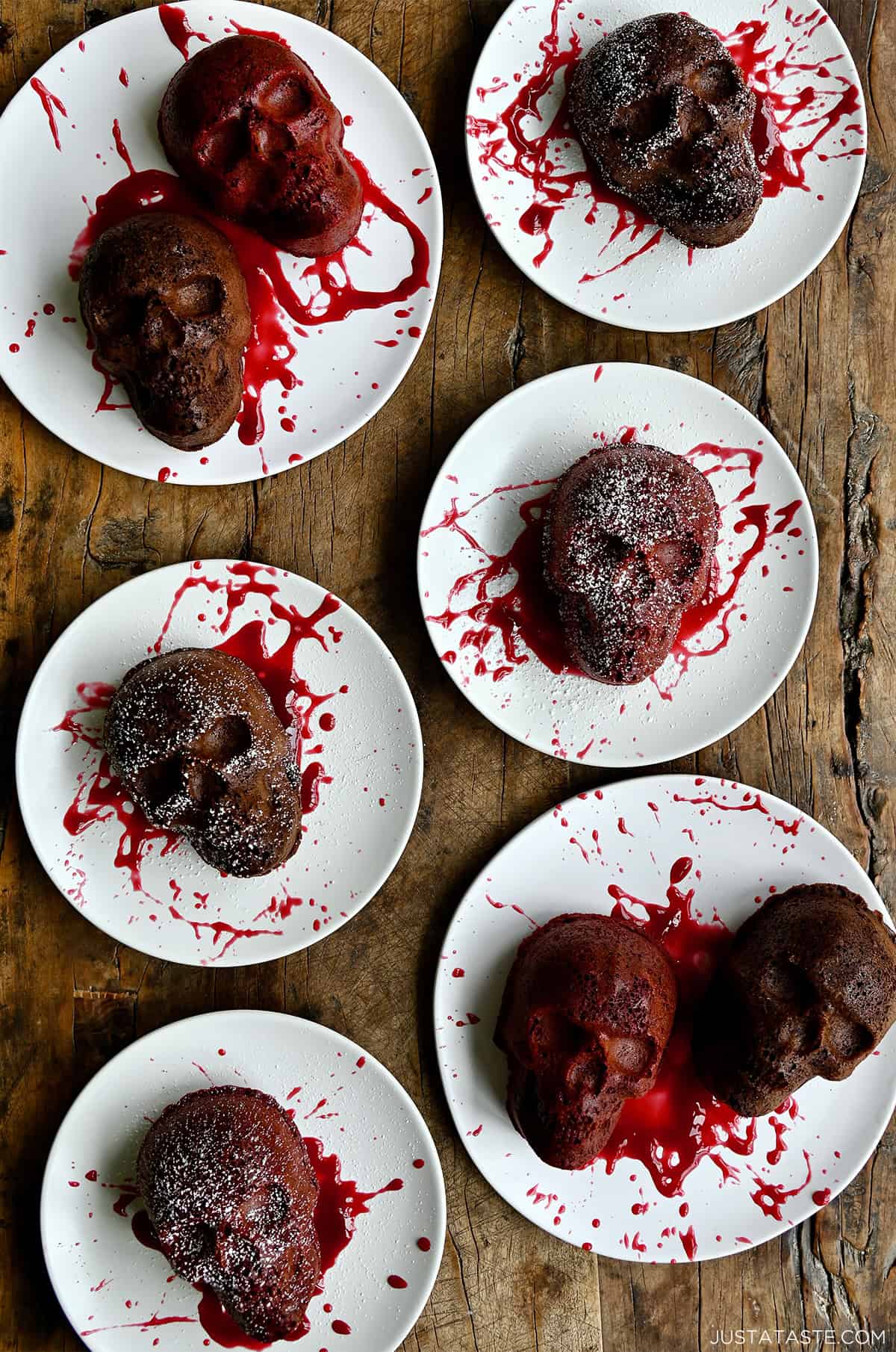 Mini Halloween cakes on plates with a splatter of raspberry sauce and a dusting of powdered sugar.
