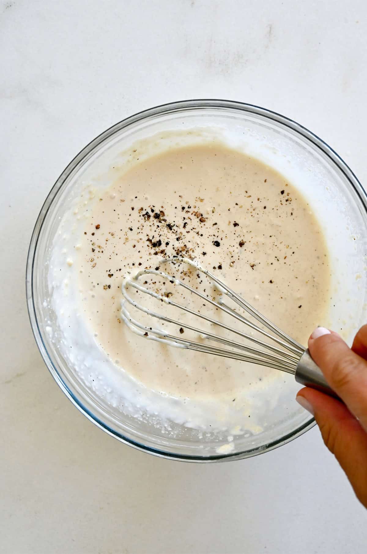 Whisking together homemade Caesar dressing in a large bowl.