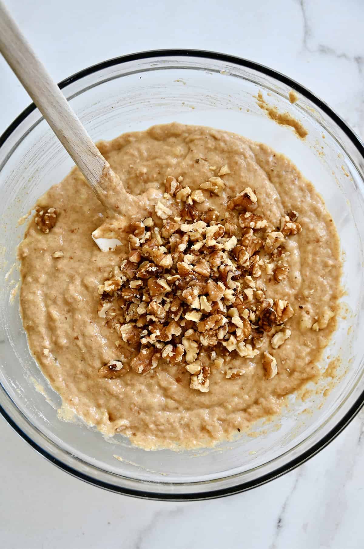 Folding chopped walnuts into a protein muffin batter in a large mixing bowl.