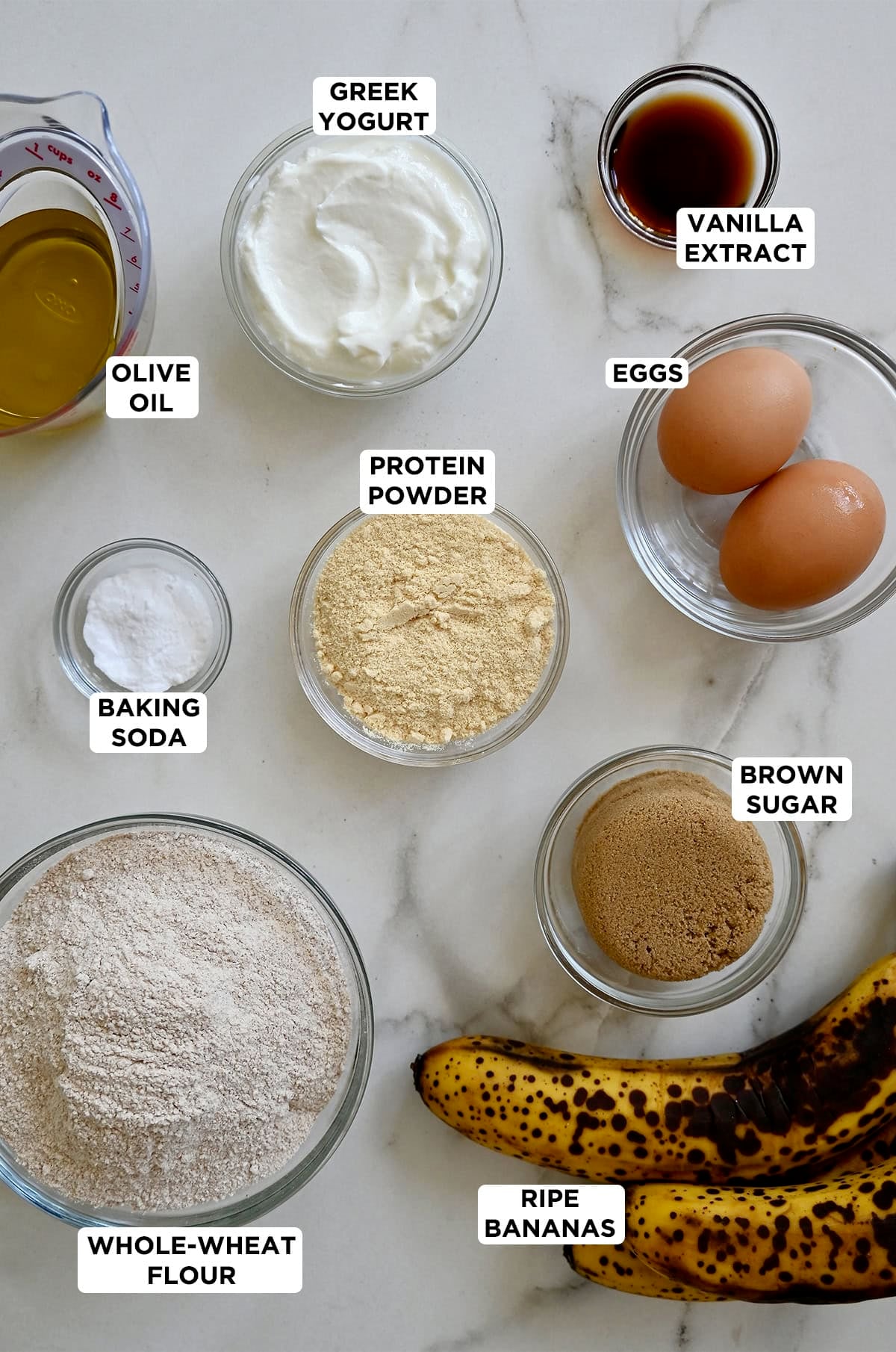 Ingredients to make banana muffins with protein powder in various sizes of prep bowls.