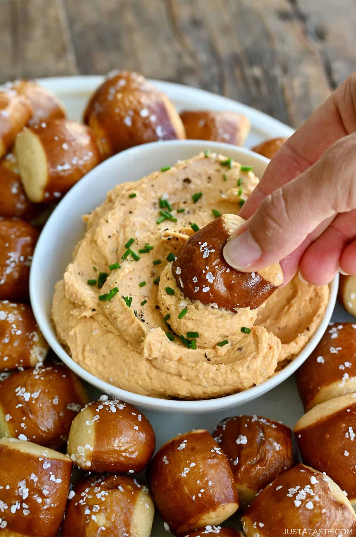 A hand dips a soft pretzel bite into homemade pub cheese in a small bowl.