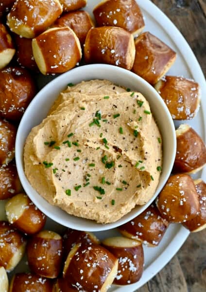 Homemade pub cheese spread in a small bowl on a plate surrounded by soft pretzel bites.
