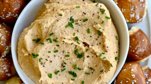 Homemade pub cheese spread in a small bowl on a plate surrounded by soft pretzel bites.