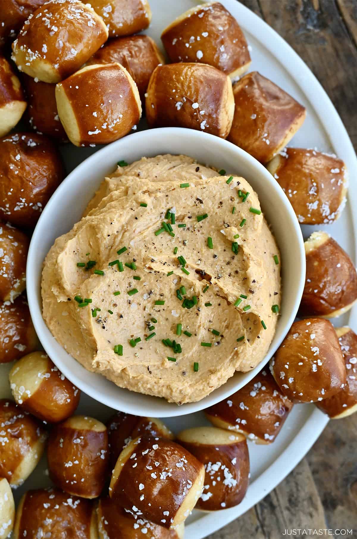 Homemade pub cheese spread in a small bowl on a plate surrounded by soft pretzel bites.