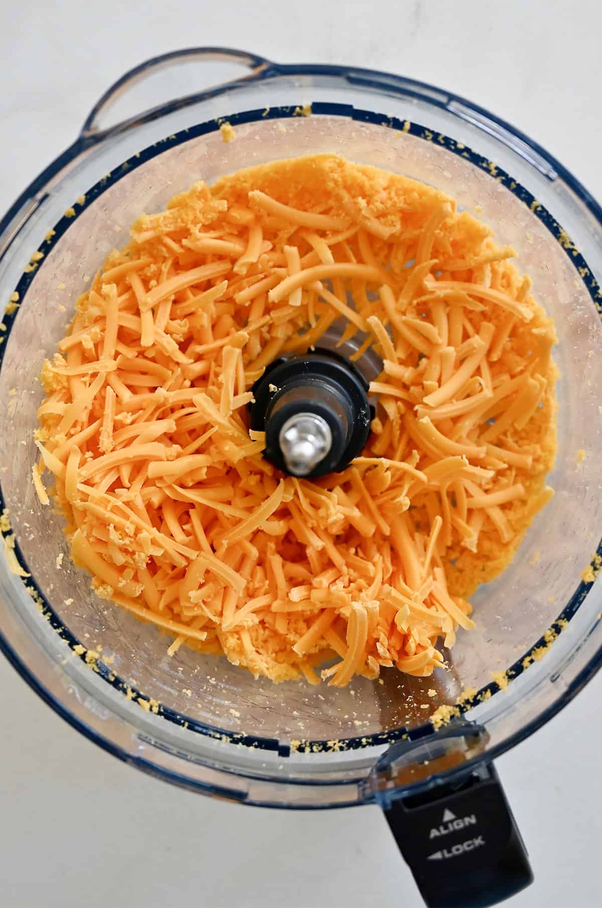 Shredded cheddar cheese in the bowl of a food processor with the shredding attachment.