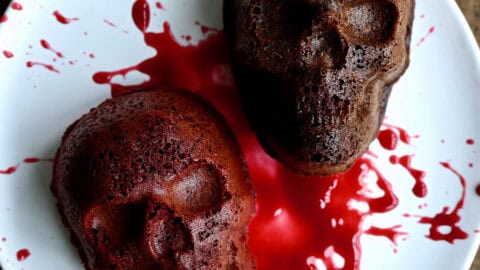 Two mini Halloween skull cakes on a plate, splattered with raspberry sauce.