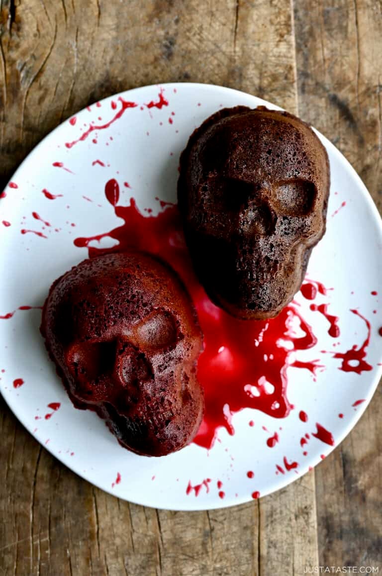 Two mini Halloween skull cakes on a plate, splattered with raspberry sauce.