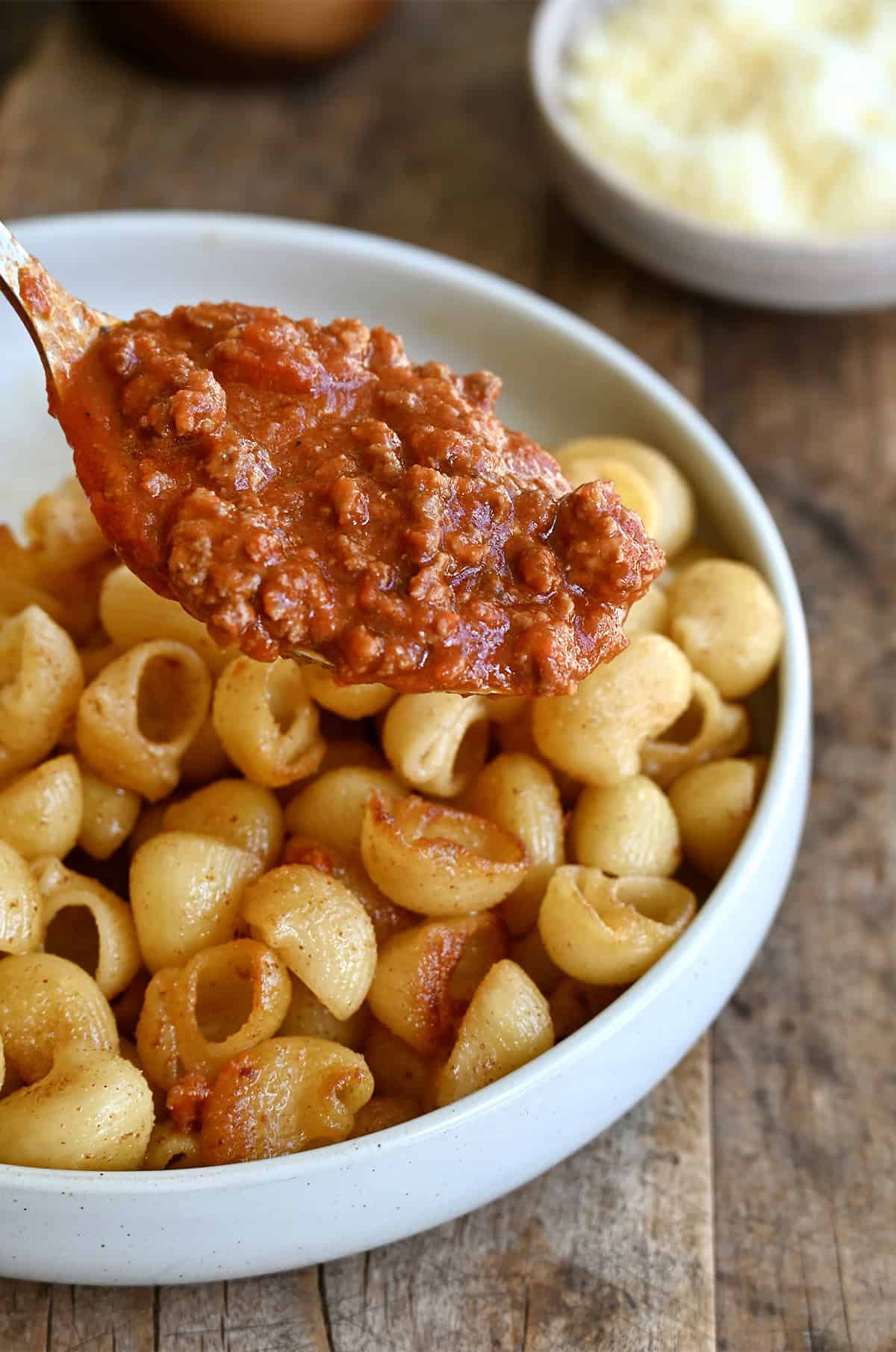 Spooning Bolognese sauce atop toasted noodles in a bowl.