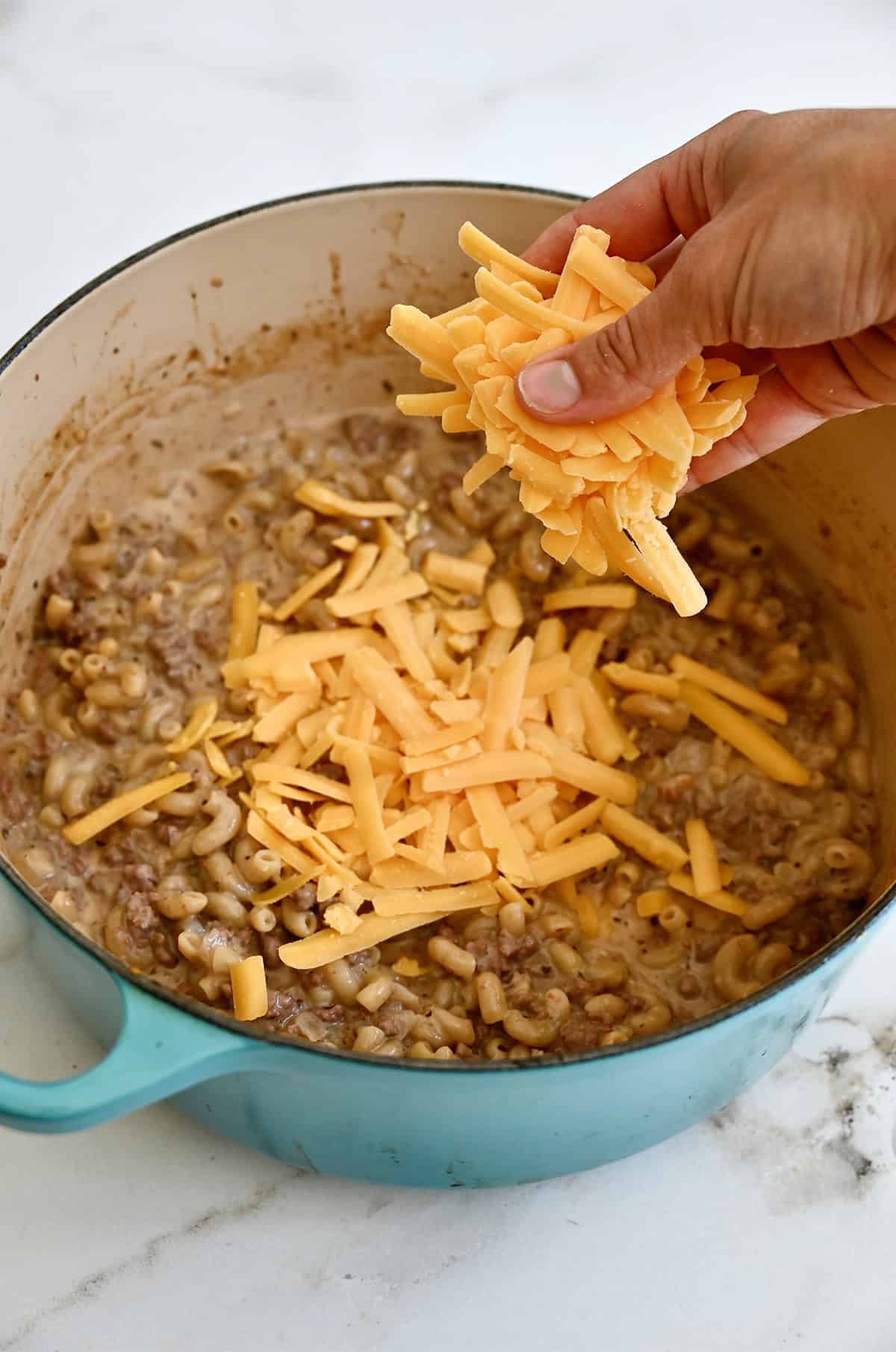 Freshly shredded cheddar cheese being added to creamy ground beef and macaroni.