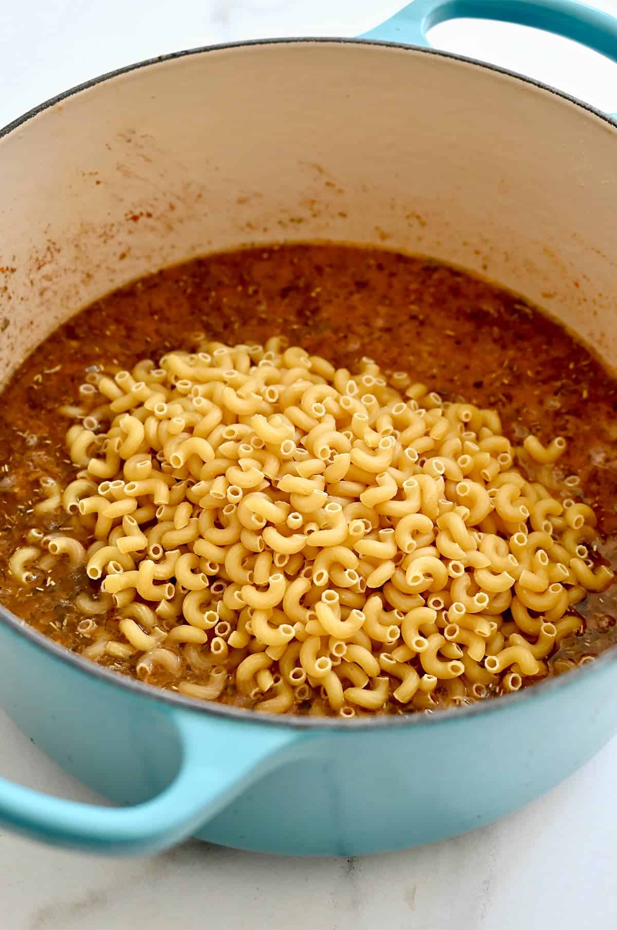 Uncooked elbow macaroni in a ground beef and broth mixture.