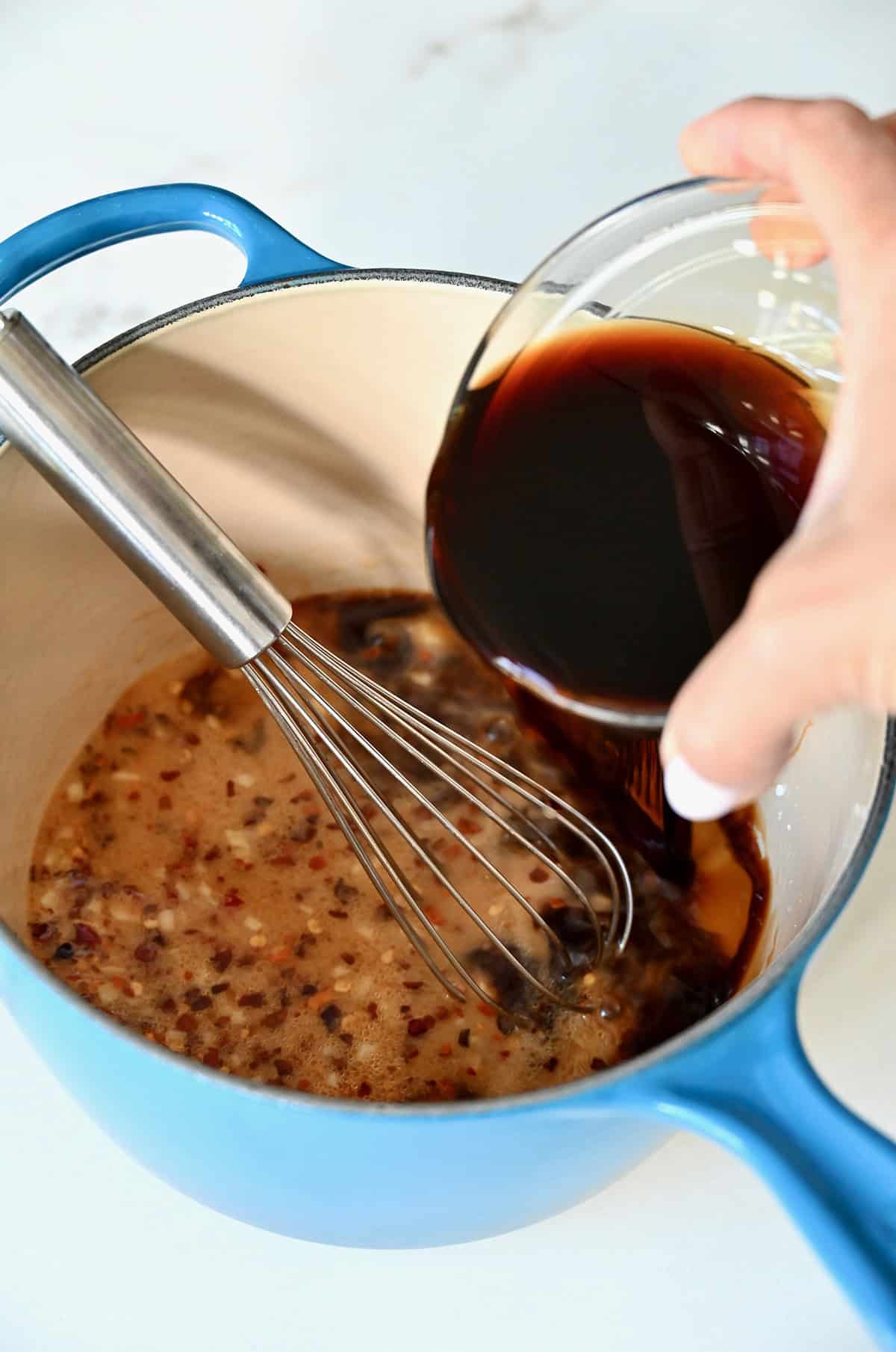 Adding low-sodium soy sauce to a small saucepan with a whisk.