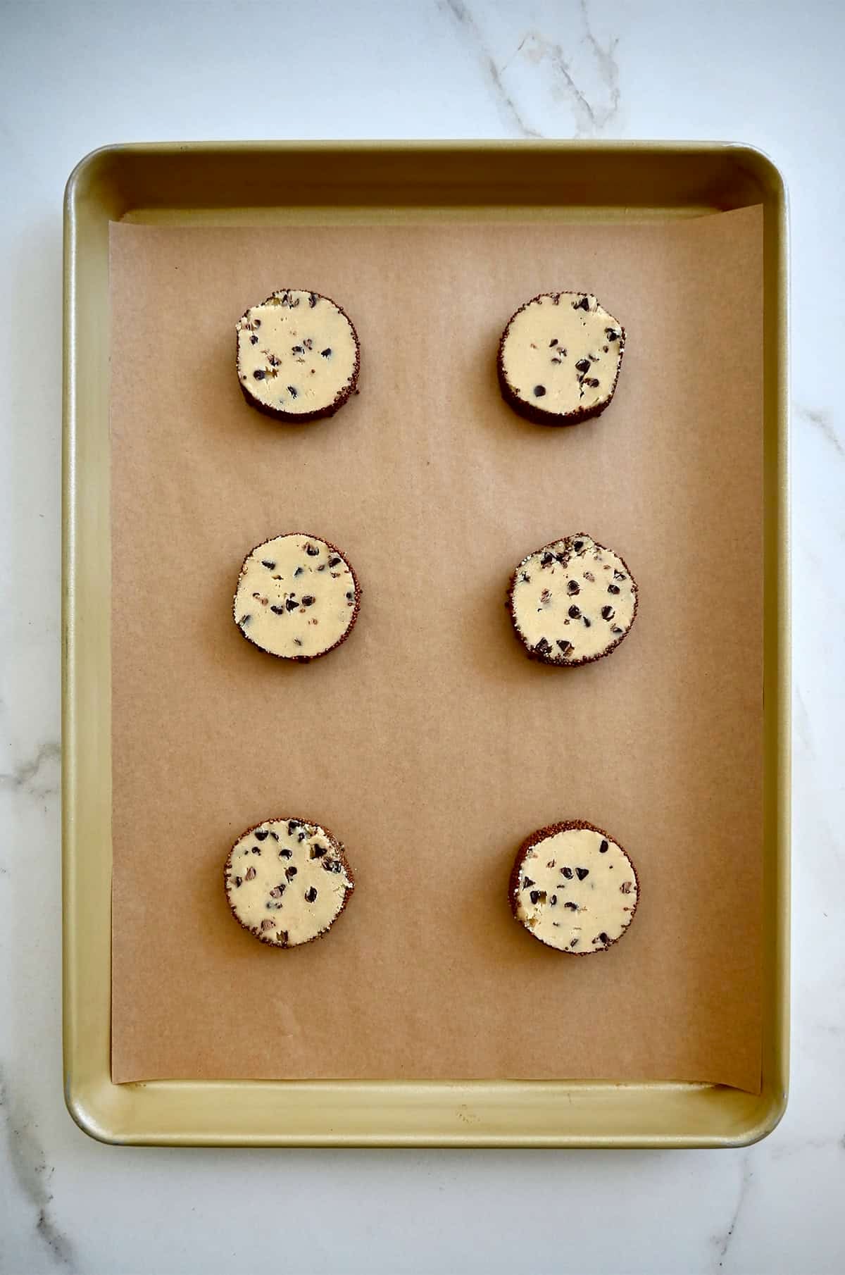 Mini chocolate chip cookie dough rounds on a parchment paper-lined baking sheet.