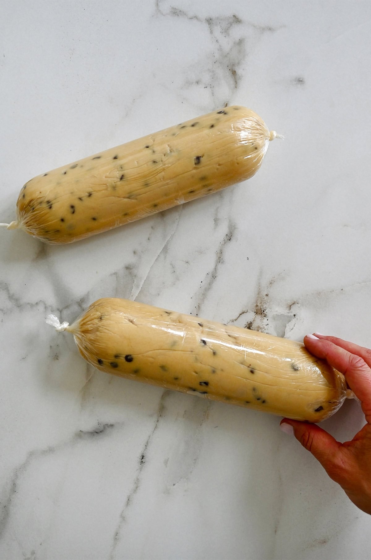 Two chocolate chip cookie dough logs securely wrapped in plastic wrap before chilling.