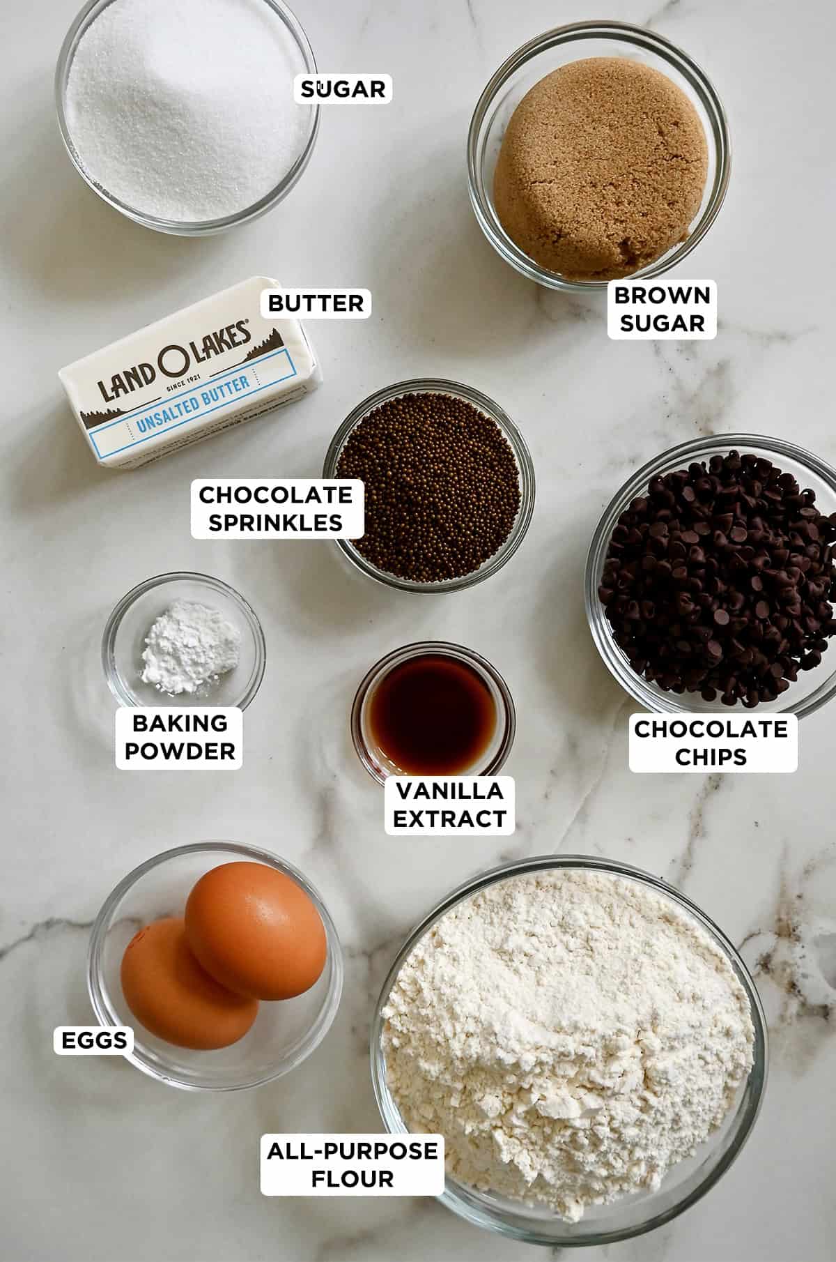 All the ingredients needed to make slice-and-bake chocolate chip cookies in glass bowls of various sizes.