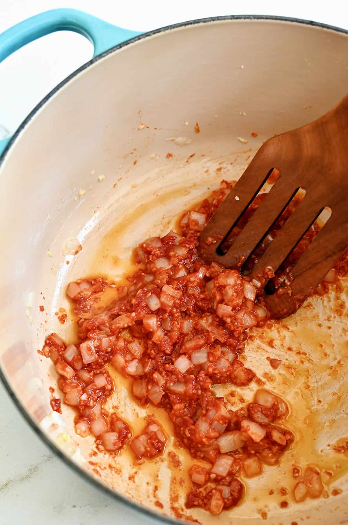 Tomato paste stirred into softened onions and garlic in a Dutch oven.
